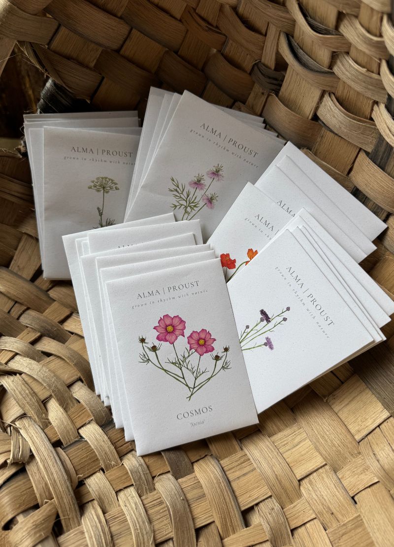 Stack of 'Alma Proust' seed packs with floral designs on a woven surface