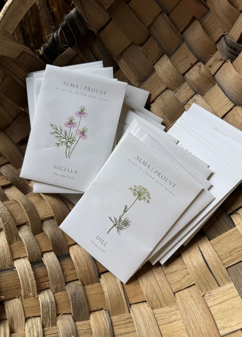Stack of 'Alma Proust' seed packs with floral designs on a woven surface