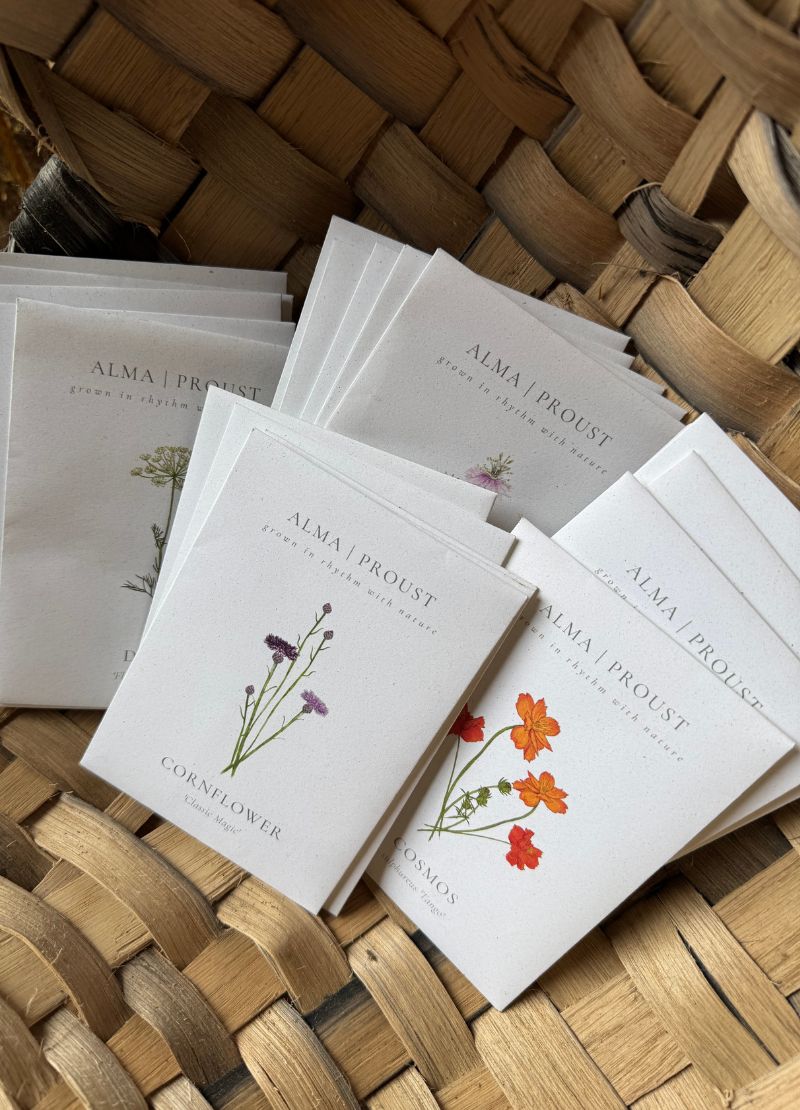 Stack of 'Alma Proust' seed packs with floral designs on a woven surface