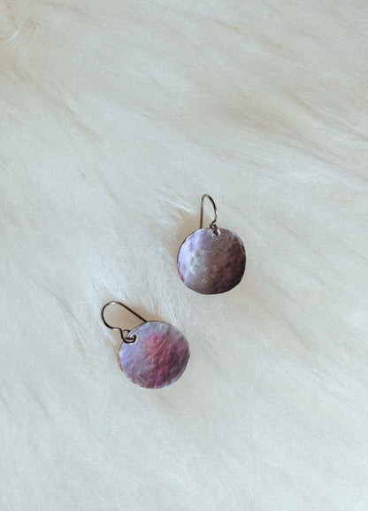 Pair of round, hammered metal earrings on a light fabric background
